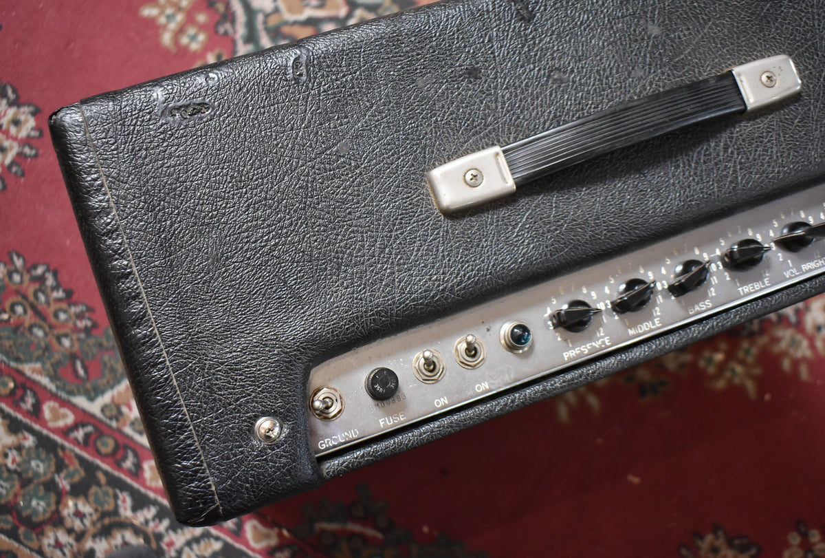 Close-up of the amp's top, showing the black tolex with scuffs and a tear, a silver control panel with black knobs, and a black handle.
