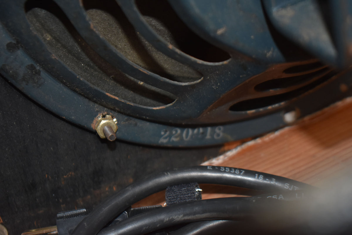 Close-up of a dark gray speaker with a visible mounting bolt, showing the stamped number "220918" and black cables below.