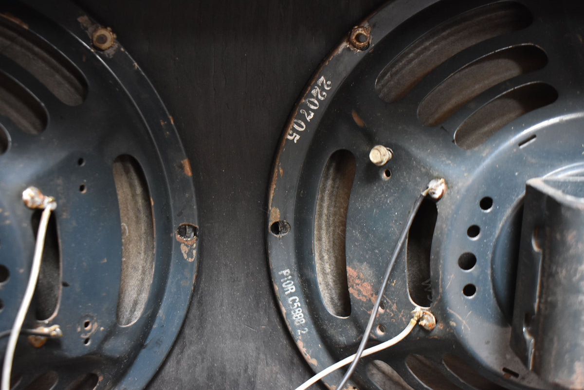 Close-up of two dark grey speakers with visible rust on the frames, showing wiring and stamped numbers on the right speaker.