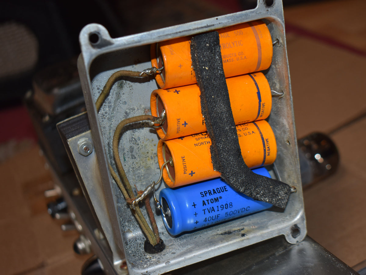 Close-up of the amp's chassis, showing three orange capacitors and one blue capacitor, wired together in a corroded metal box.