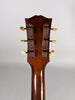The guitar's dark brown headstock and neck are viewed from behind, showing six cream-colored tuning pegs with worn metal plates.