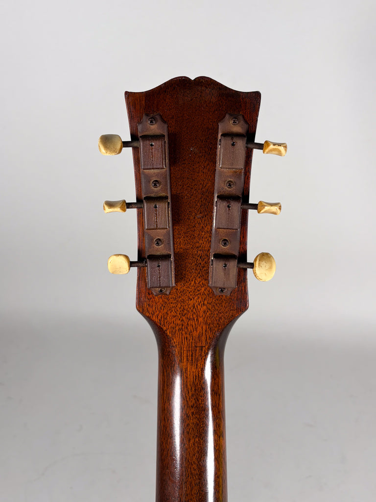 The guitar's dark brown headstock and neck are viewed from behind, showing six cream-colored tuning pegs with worn metal plates.