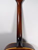 The guitar's dark brown neck and heel are visible from the back, joining a dark sunburst body with cream binding.