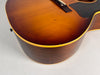 Close-up of the sunburst acoustic guitar's lower bout, showing the dark brown sides, light binding, and some finish wear on the top.