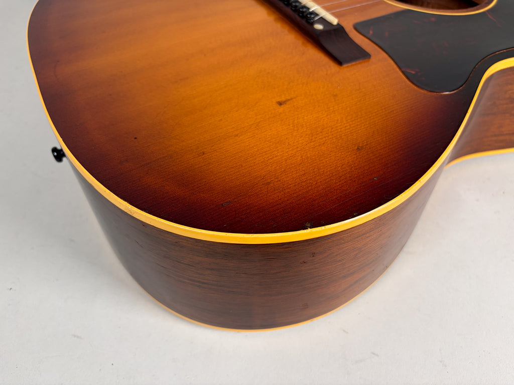 Close-up of the sunburst acoustic guitar's lower bout, showing the dark brown sides, light binding, and some finish wear on the top.