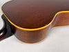 Close-up of the guitar's lower bout and neck heel, showing dark brown wood grain, yellow binding, and a small chip on the body.