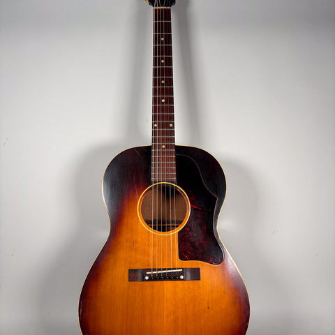 Full-length view of a sunburst acoustic guitar with a dark tortoiseshell pickguard, showing wear and finish checking.