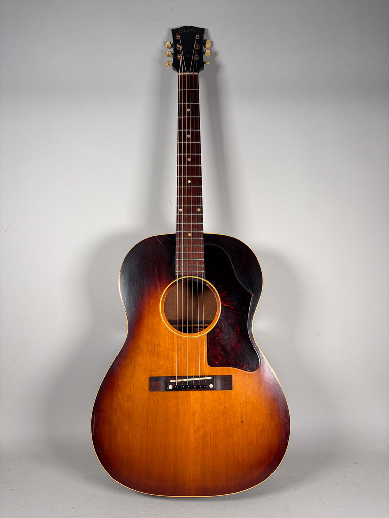 Full-length view of a sunburst acoustic guitar with a dark tortoiseshell pickguard, showing wear and finish checking.