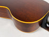 Close-up of the dark brown acoustic guitar's lower bout and side, showing the light yellow binding and some finish wear near the neck joint.