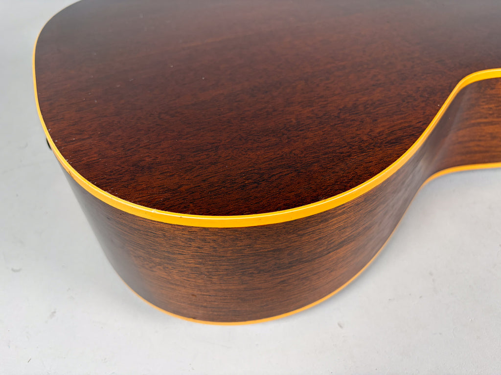 Close-up of the guitar's dark brown body, showing the wood grain and yellow binding along the top and side edges, with minor wear.