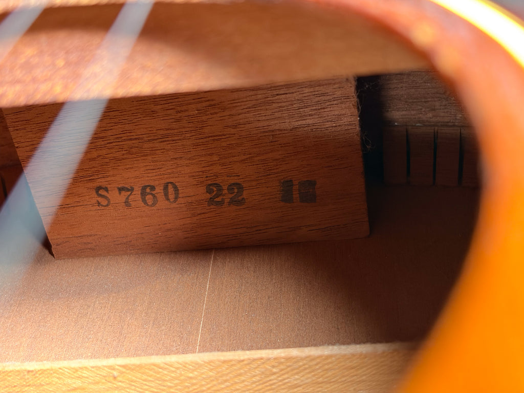 Inside the guitar's soundhole, a light brown wooden brace with "S760 22" stamped in black is visible, along with other internal bracing.