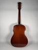Full rear view of the dark brown acoustic guitar, showing the body's wood grain, light binding, and six gold tuners on the headstock.