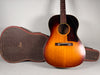 Full-front view of the sunburst acoustic guitar, showing its dark tortoiseshell pickguard, rosewood bridge, and open alligator-skin case.