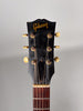 The guitar's black headstock, with gold lettering and six cream tuning pegs, shows significant wear and finish checking.