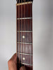 Close-up of the dark brown fretboard, showing the first five frets, dot inlays, and a hand holding the neck.