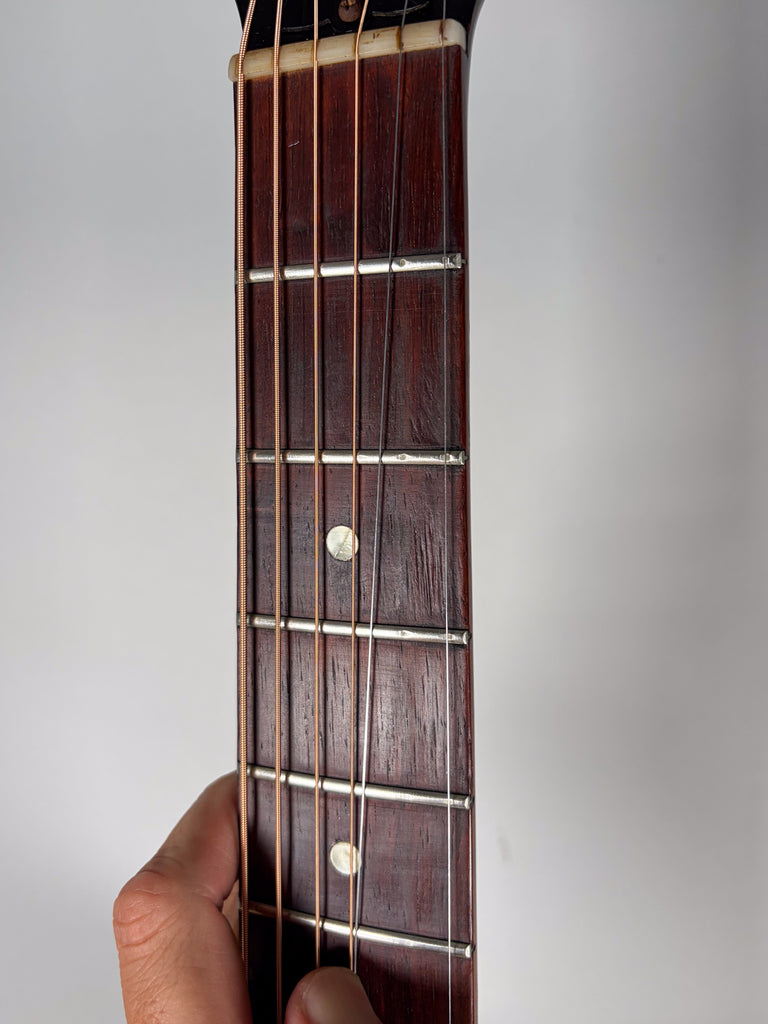 Close-up of the dark brown fretboard, showing the first five frets, dot inlays, and a hand holding the neck.