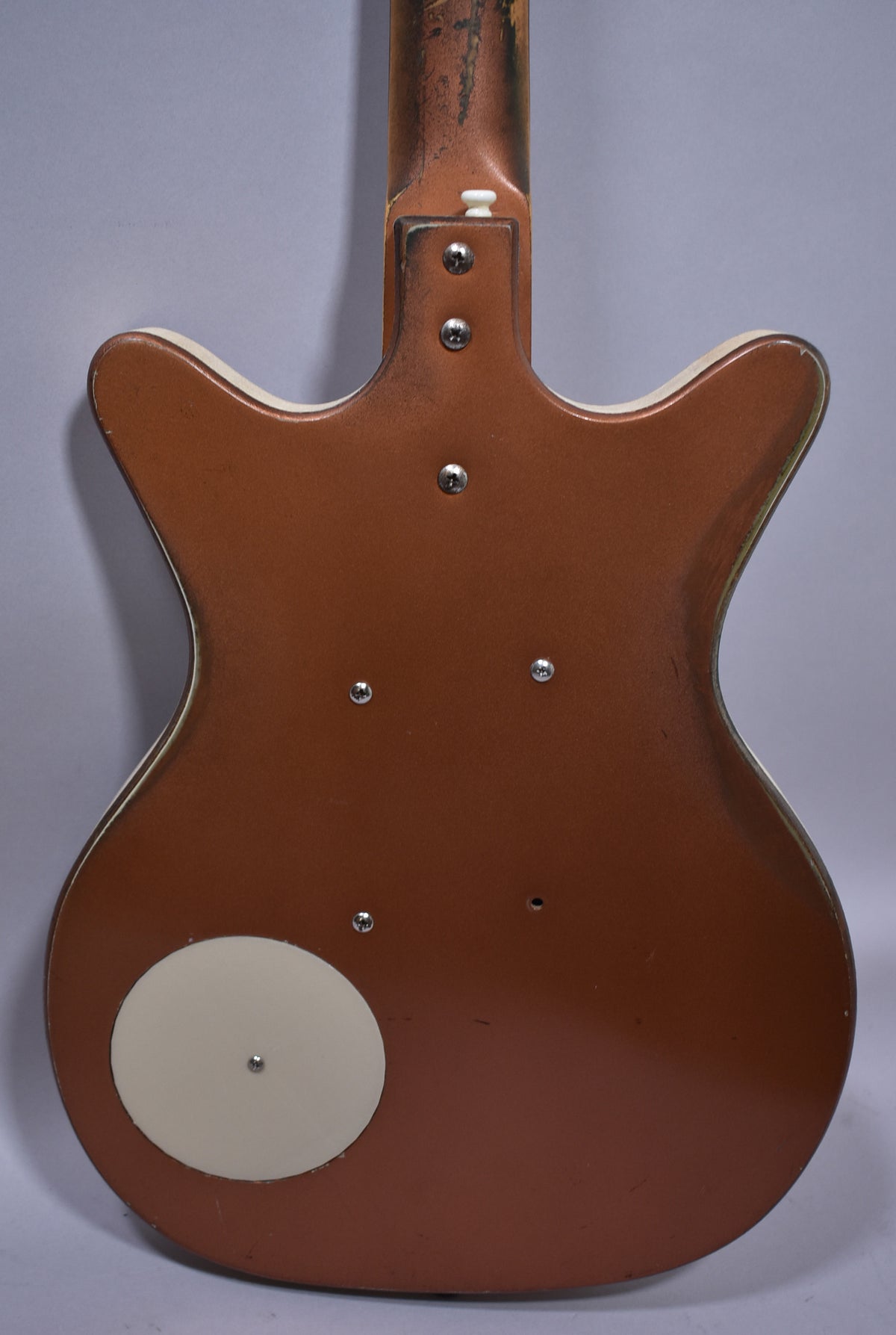 The guitar's copper back shows a circular cream control plate, a worn neck joint, and a white binding with visible wear.