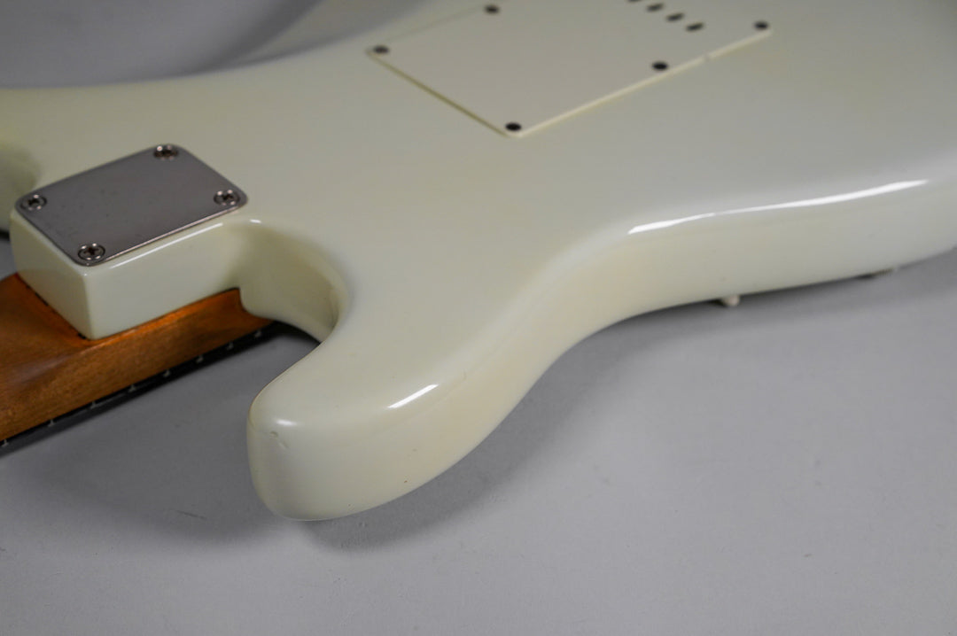 The back of a white electric guitar body, showing the neck plate, tremolo cover, and some finish wear.
