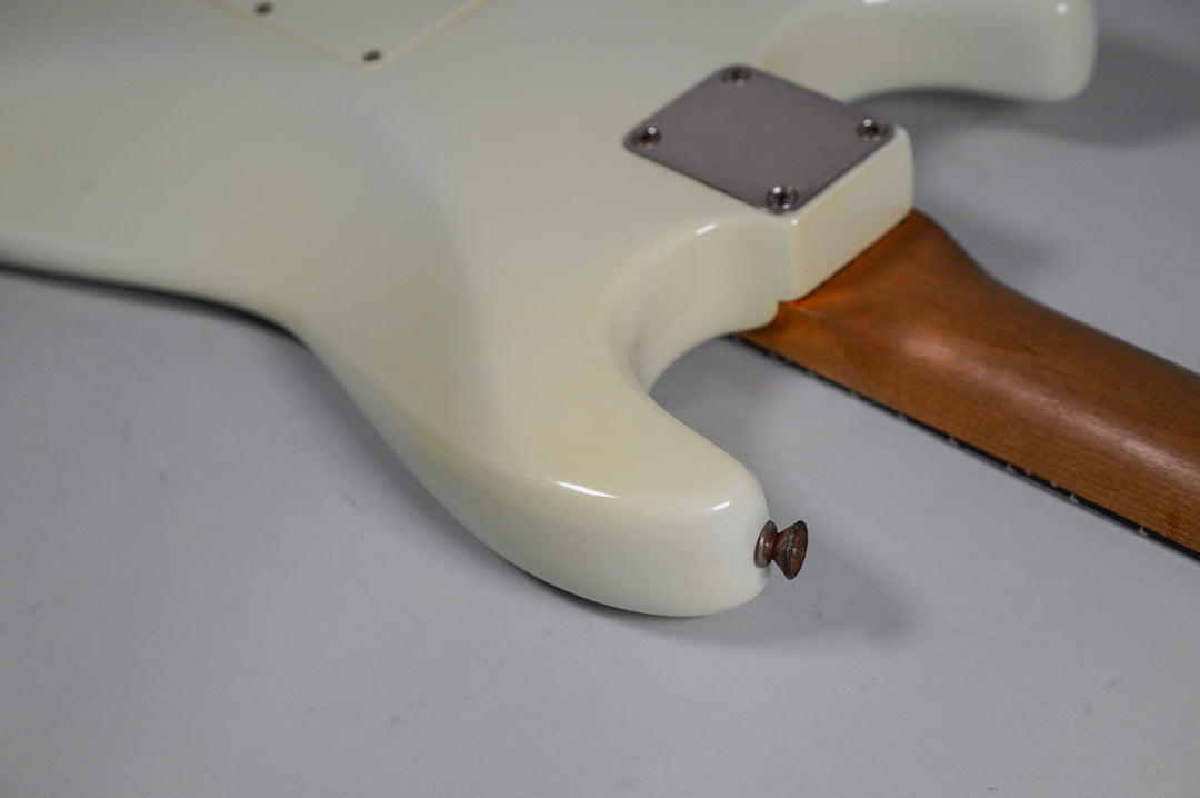 The white refinished body, with a shiny finish and some minor wear, meets the neck at a chrome plate.