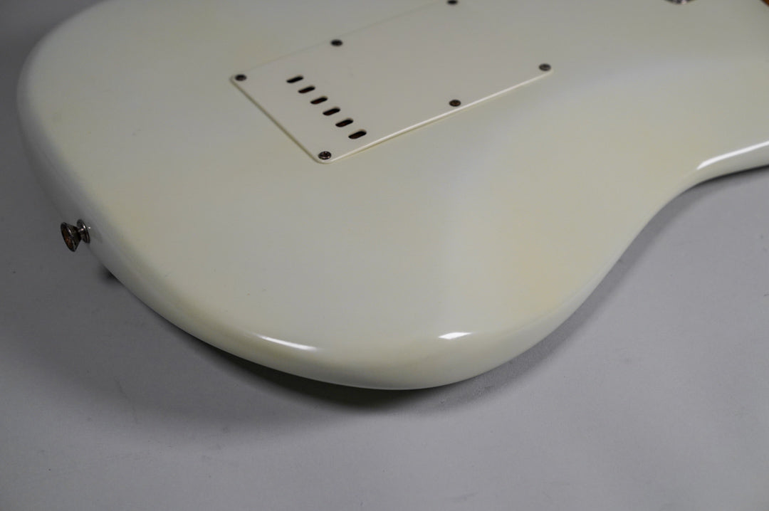 The back of the white refinished guitar body, showing the tremolo cavity cover, strap button, and some finish checking.