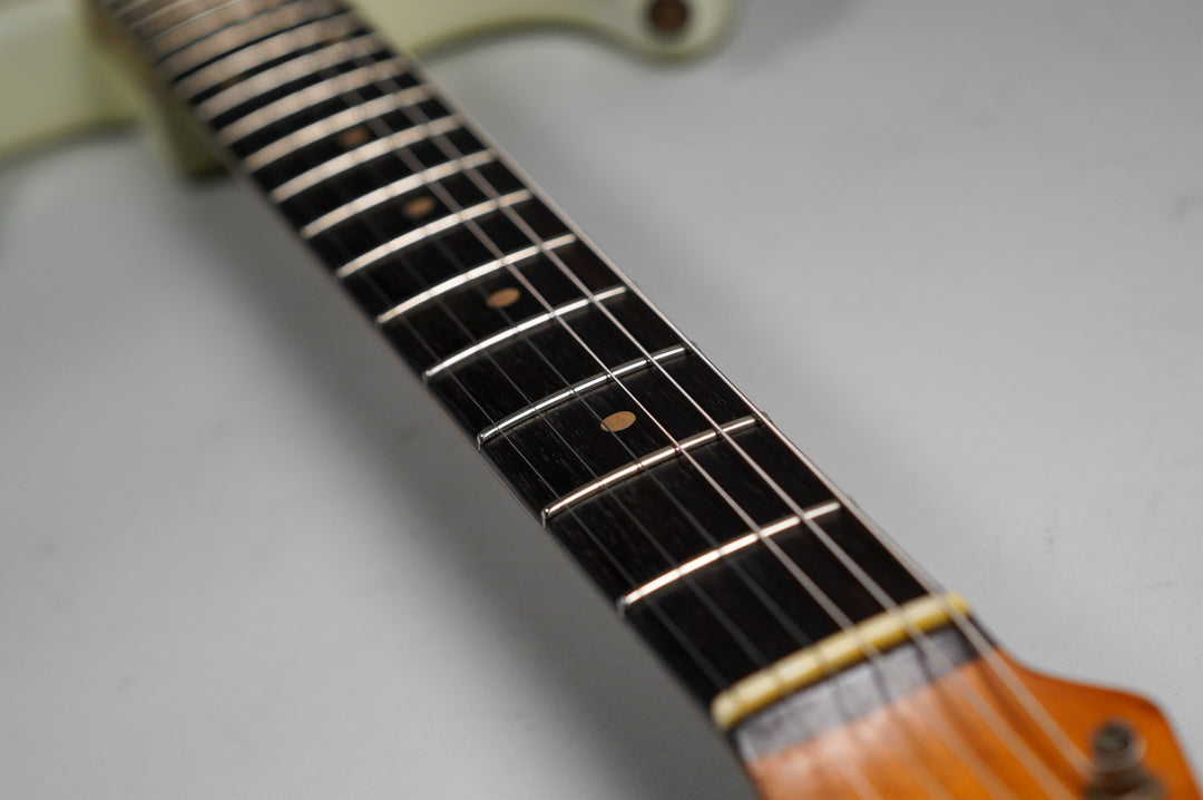Close-up of the dark fretboard with light frets and dot inlays, showing the cream-colored nut and part of the light-colored headstock.