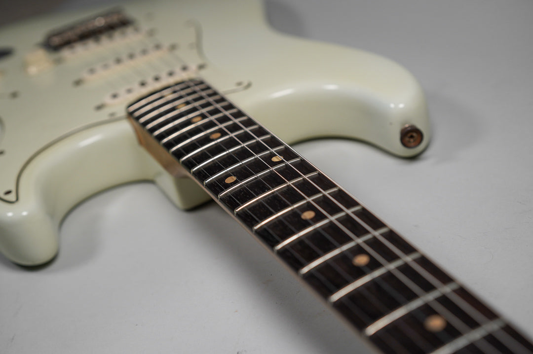 Close-up of the white guitar body and dark fretboard with dot inlays, showing wear on the strap button and body edge.