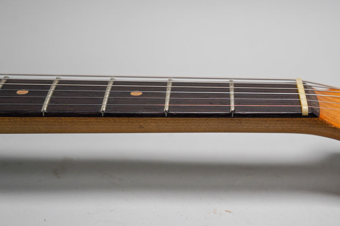 Close-up of the guitar's dark fretboard with light frets and dot inlays, showing a cream nut and light wood neck.