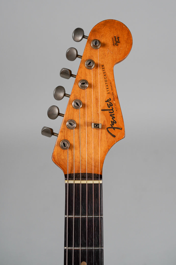 The guitar's headstock and upper fretboard are visible, showing a worn, ambered finish and six aged metal tuners.