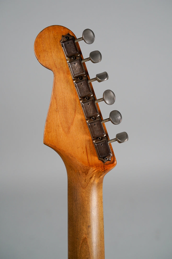The back of a worn, light brown wooden headstock and neck, with six tarnished metal tuners visible on the right.