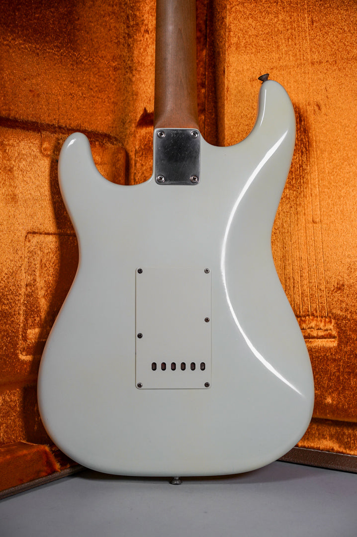The white refinished Stratocaster's back shows a neck plate, tremolo cover, and strap button, with minor finish wear.