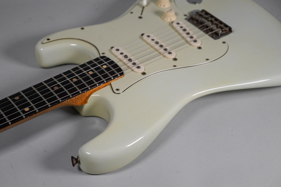 Upper body of a white electric guitar with a dark fretboard, three single-coil pickups, and a worn bridge.