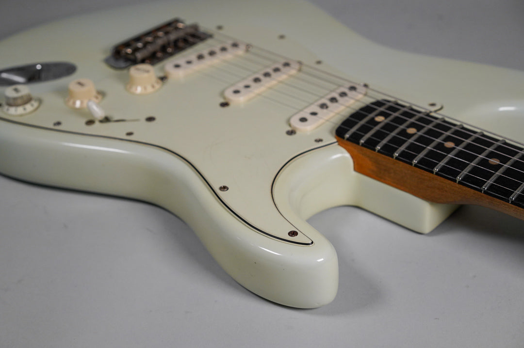 The white electric guitar's body, pickguard, and controls are visible, with light checking and wear on the glossy finish.