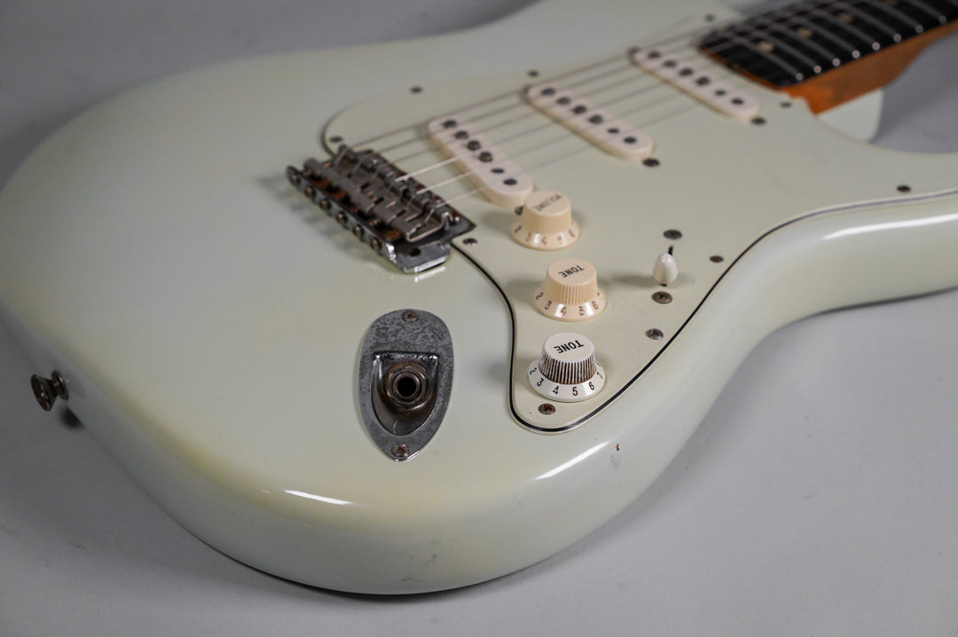 Close-up of the guitar's lower body, showing the off-white finish, aged cream pickguard, controls, and input jack with visible wear.