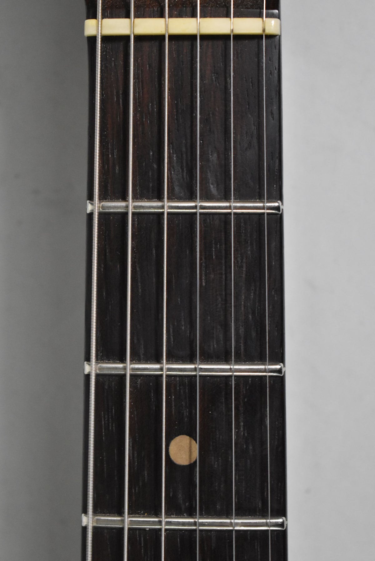 Close-up of the dark rosewood fretboard, showing the cream nut, silver frets, strings, and a light brown dot inlay at the 7th fret.