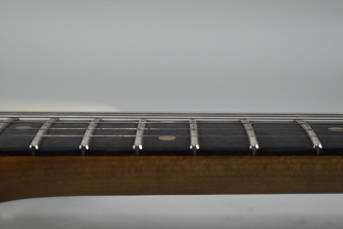 Close-up of the guitar's dark fretboard and frets, with a few light circular inlays visible, against a light background.