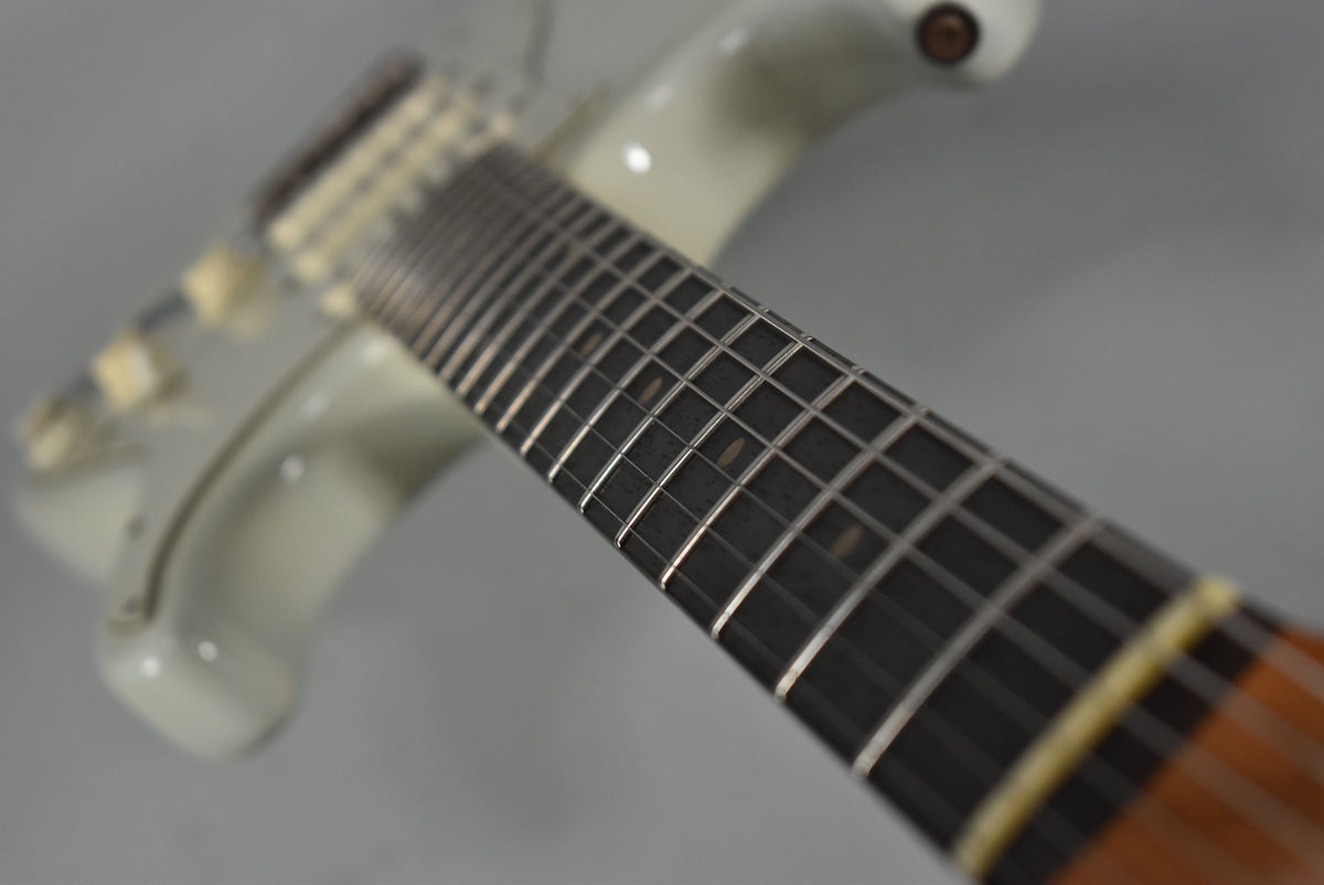 Close-up of the guitar's dark fretboard with rectangular inlays, showing light fret wear and a white refinished body in the background.