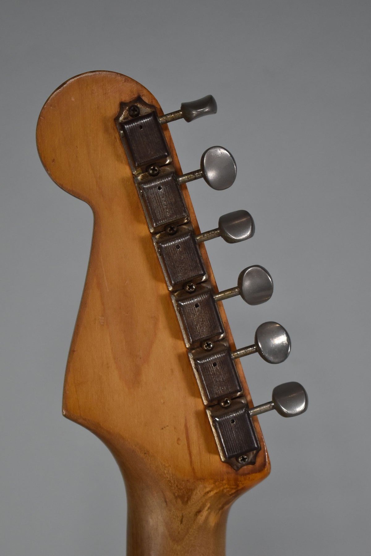 Rear view of the guitar's headstock and neck, showing six worn, rectangular tuners with oval buttons on the light brown wood.