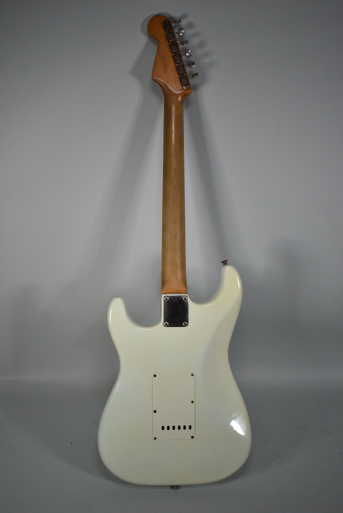 Full rear view of a white electric guitar with a light brown neck, chrome tuning pegs, and a rectangular tremolo cover.