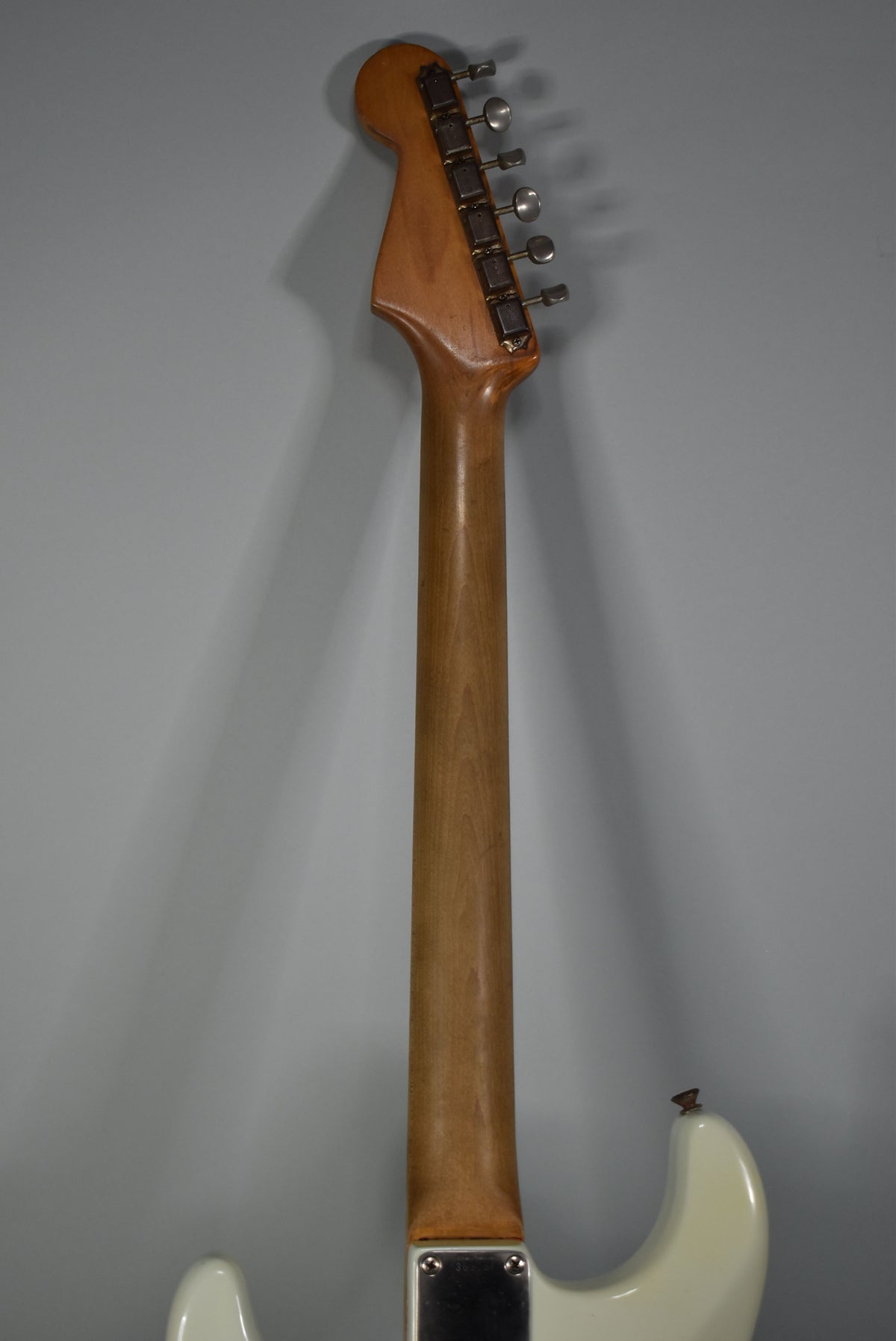 The guitar's light brown neck and headstock are viewed from behind, showing six tarnished tuners and a white body.
