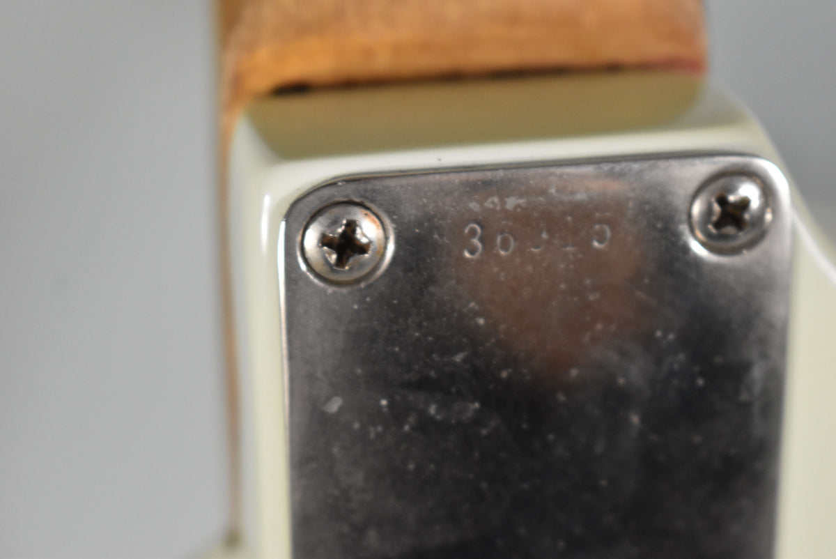 Close-up of the guitar's neck plate, showing two screws, a faint "30310" serial number, and light wear on the chrome.