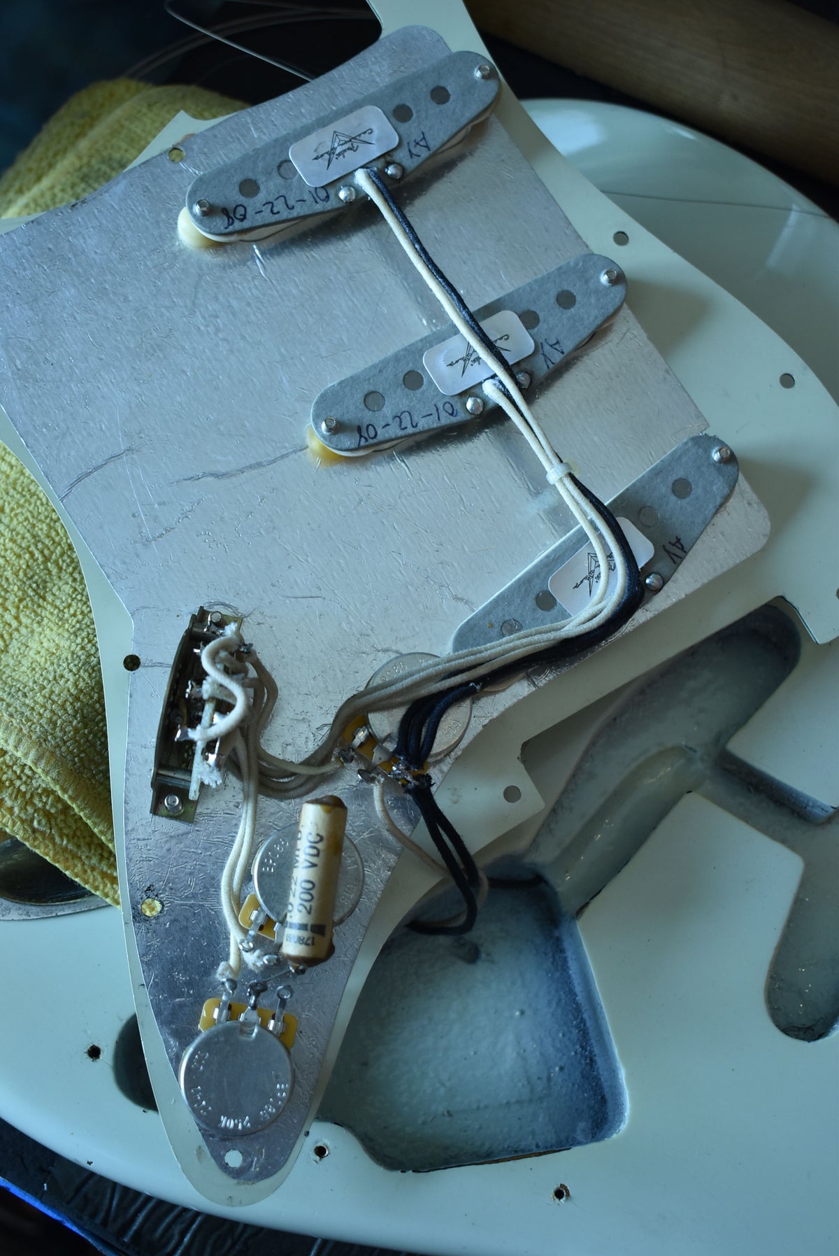 Close-up of the guitar's internal wiring, showing three pickups, a capacitor, and control pots on a metal plate.