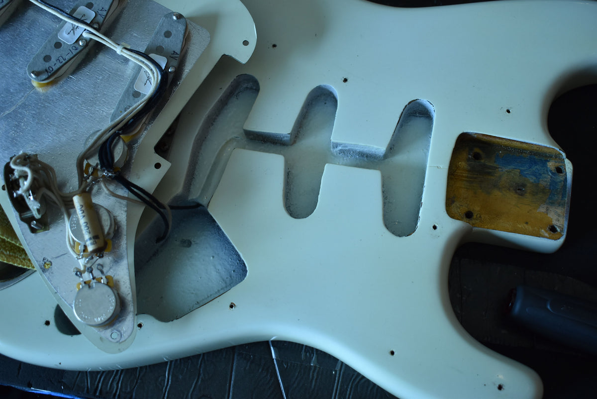 Close-up of the guitar's white body with the pickguard removed, revealing the wiring, control pots, and pickup cavities.