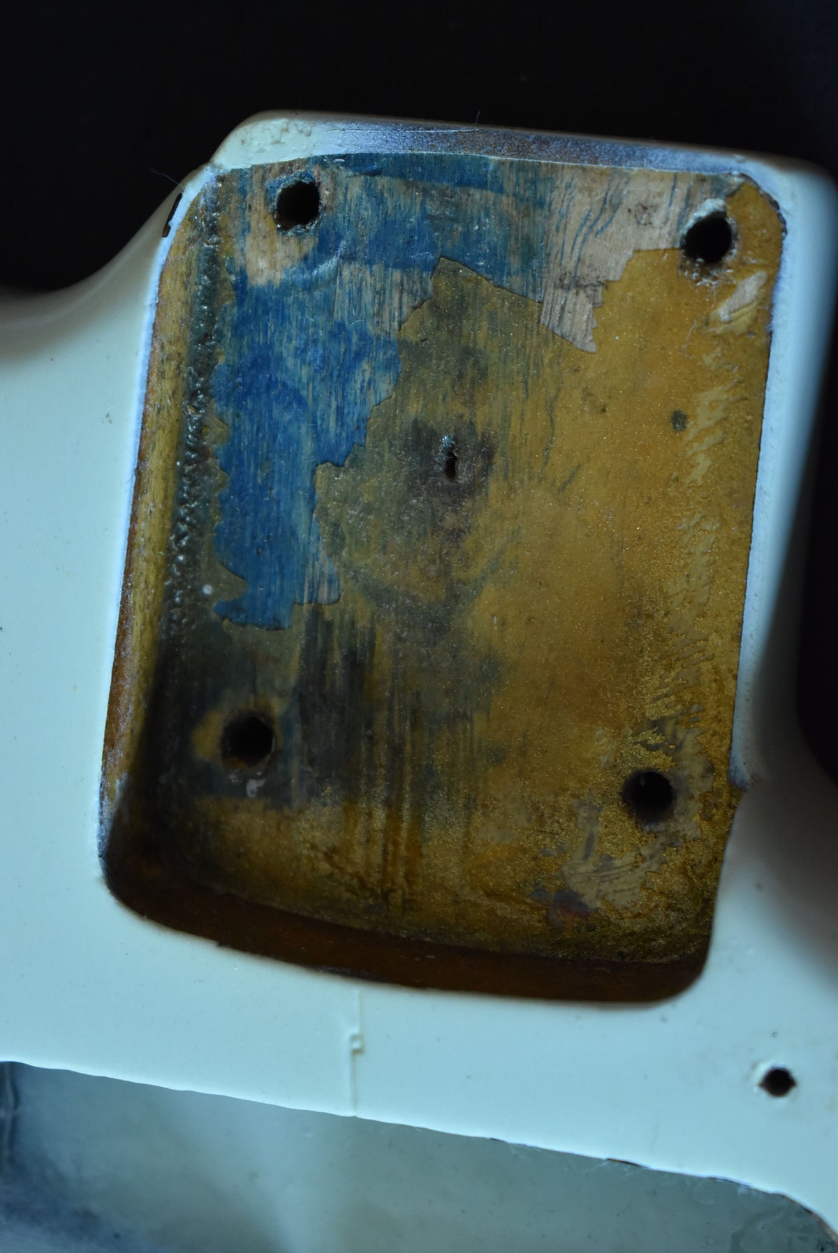 Close-up of the guitar's neck pocket, revealing worn wood with remnants of blue and gold finish, and four screw holes.
