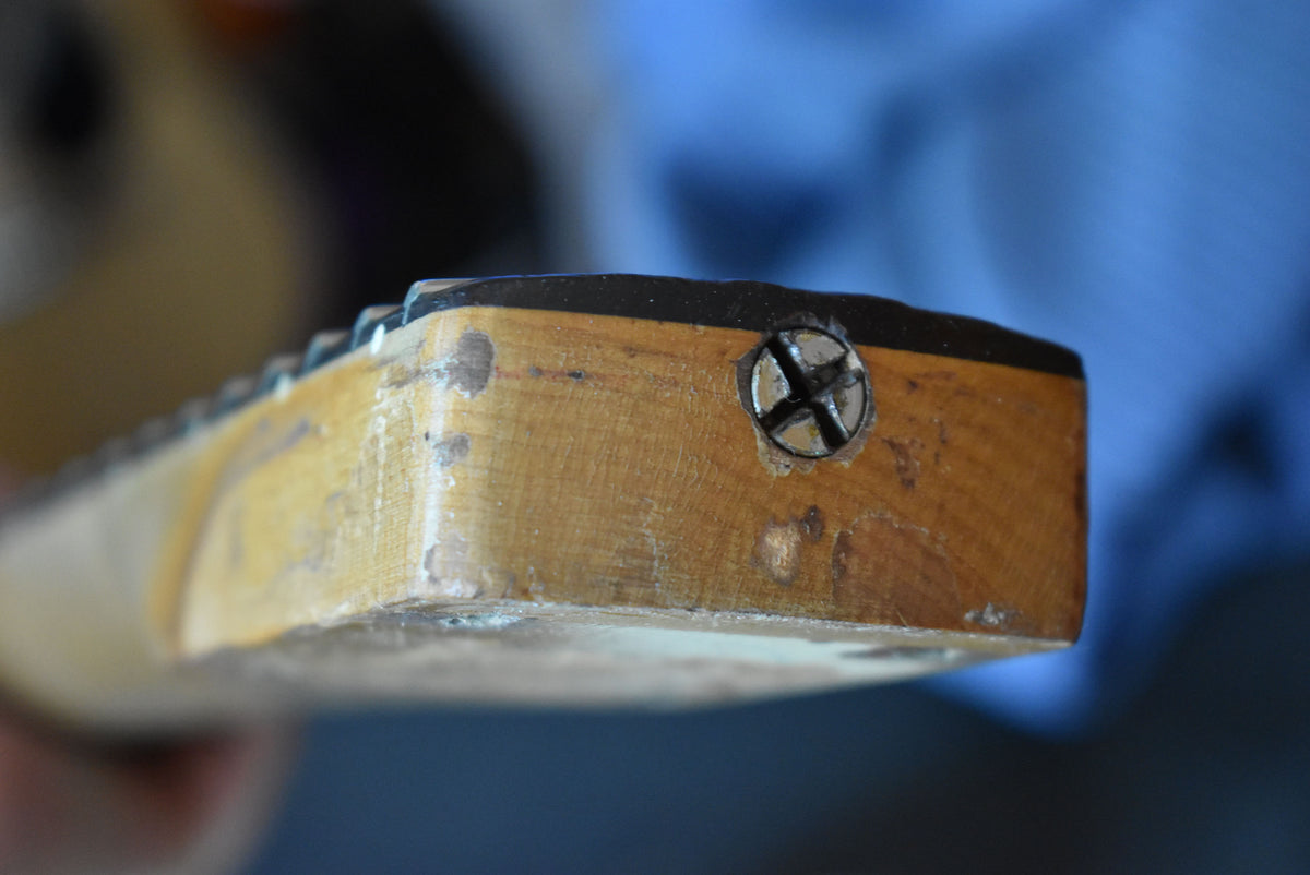Close-up of the guitar neck heel, showing a large screw, worn wood grain, and chipped finish along the edges.