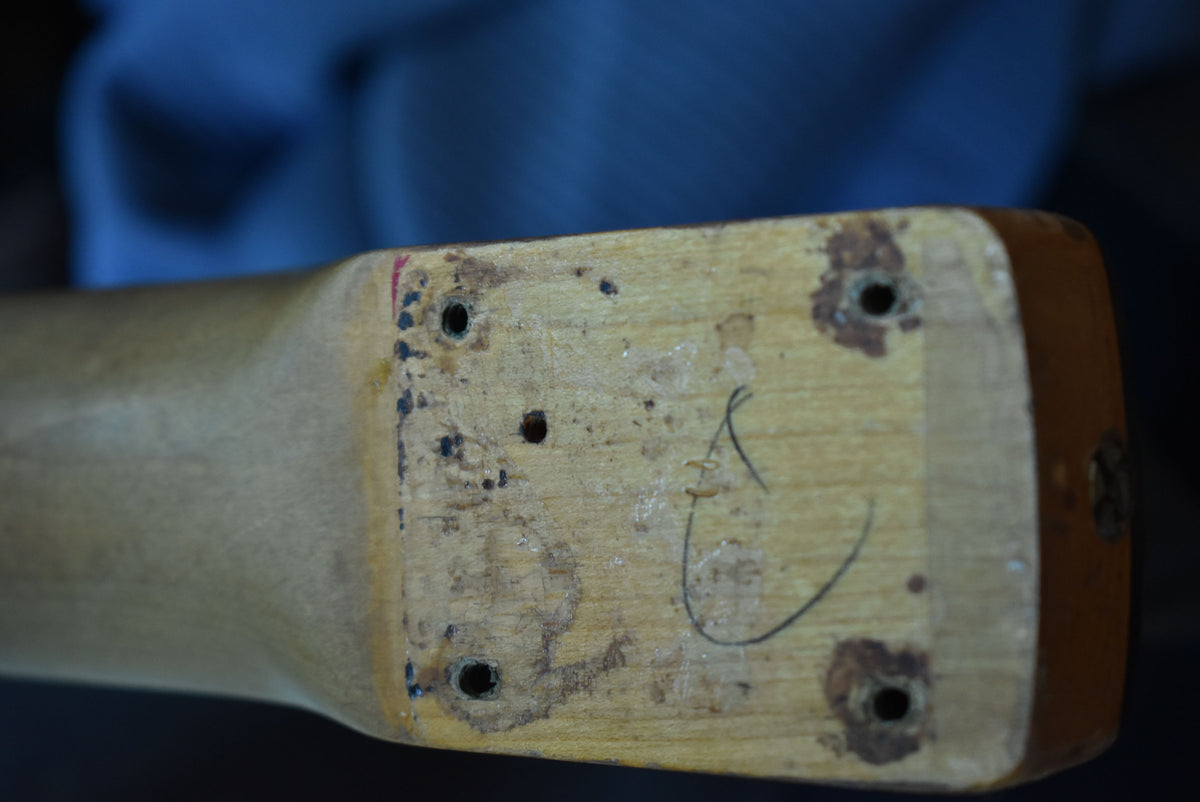 Close-up of the guitar neck heel, showing four screw holes, worn wood, and a faint "A" marking.