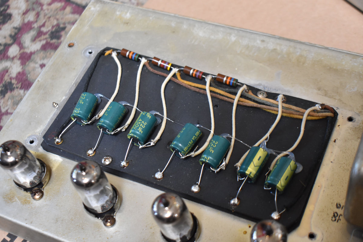 Close-up of the amp's internal circuitry, showing a row of green capacitors and resistors wired to a black board, with vacuum tubes below.