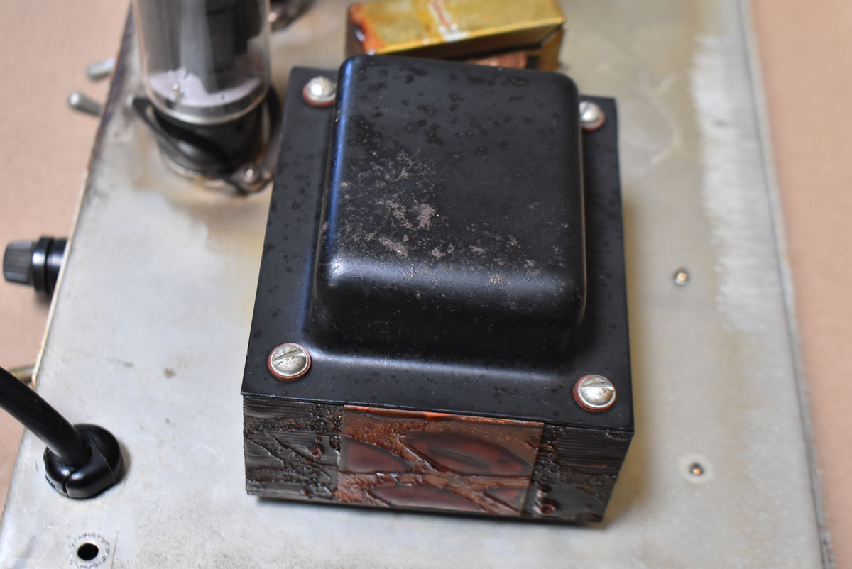 Close-up of the amp's chassis, showing a black transformer with worn paint and exposed copper windings, secured by four screws.