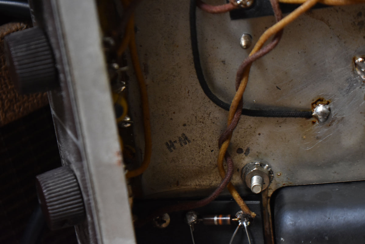 Close-up of the amplifier's internal wiring and components, showing a dirty metal chassis, two dark ribbed knobs, and a visible resistor.
