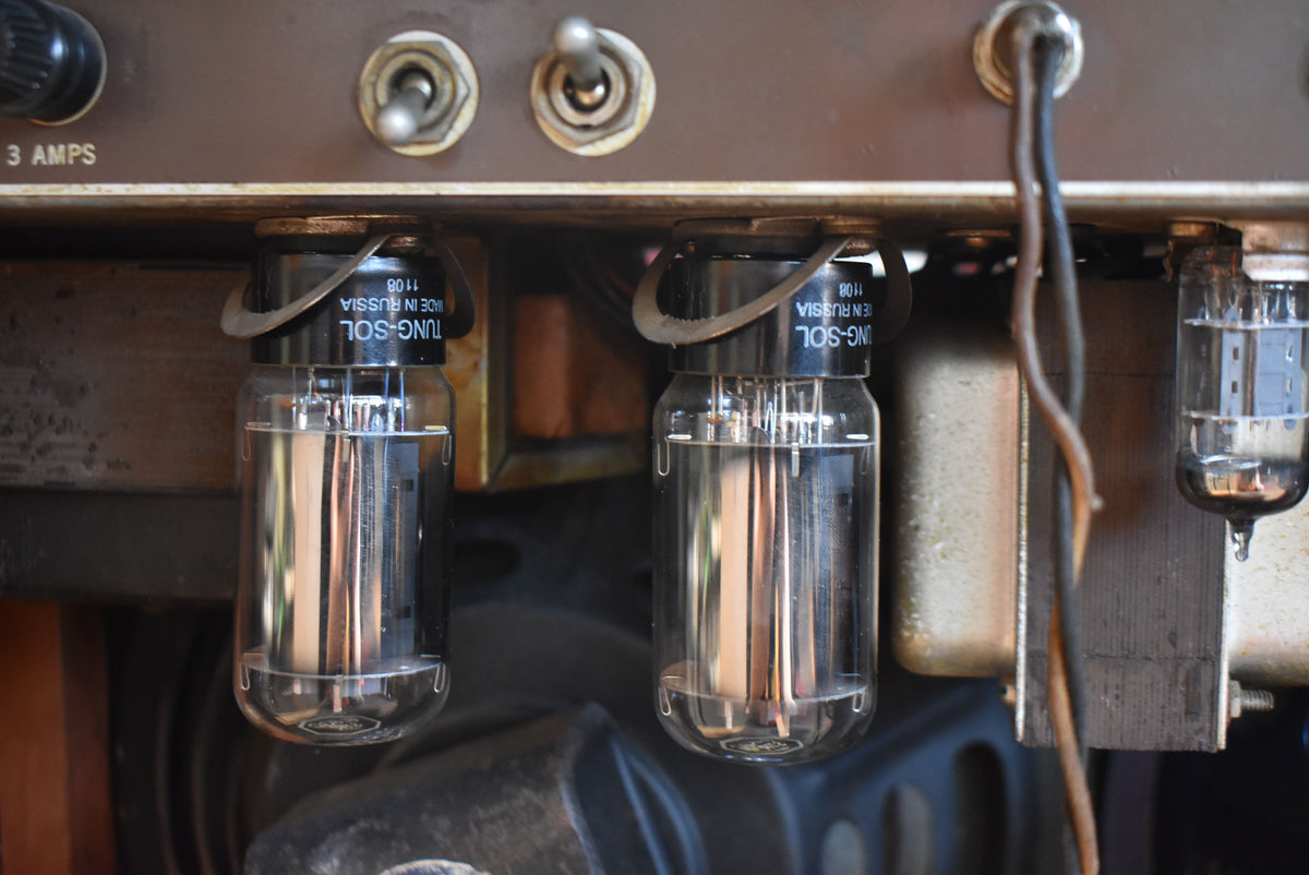 Close-up of the amplifier's rear panel, showing two large glass vacuum tubes, three metal toggle switches, and exposed wiring.