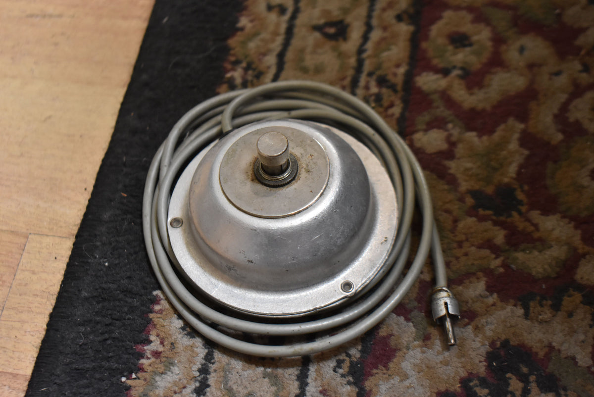 Top-down view of a vintage silver footswitch with a single button, connected to a coiled grey cable with a worn metal jack.